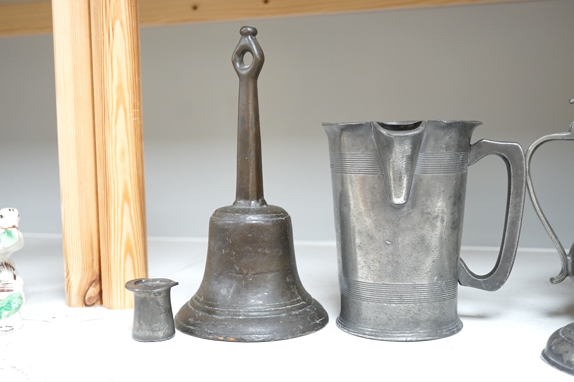 Six items of 18th century and later pewter including a jug, candlesticks, a pint measure, and a bronze hand bell, 24cm high. Condition - fair.